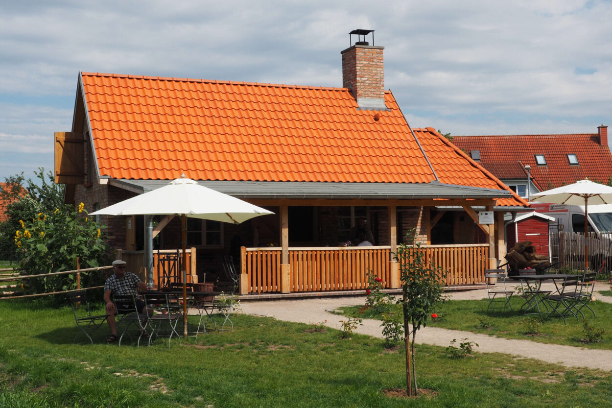 Die Bäckerei des Freilichtmuseums Kockenhagen, im Vordergrund ein Gast, der an einem Tisch unter einem Sonnenschirm sitzt