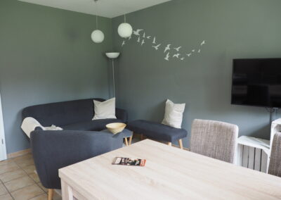 Der Wohnbereich der Ferienwohnung mit Sofa, Sessel, Sitzbank, Esstisch, Stühlen und Fernseher.