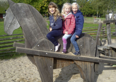 Drei Schulkinder sitzen auf einem Holzpferd.