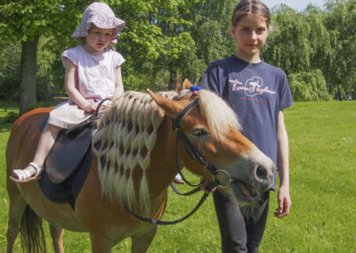 Ein junges Mädchen führt ein Kind auf einem Pony über den Museumshof.