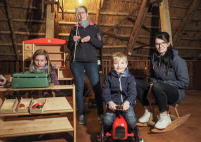 Zwei Frauen und zwei Kinder gucken auf dem Spieleboden in die Kamera.