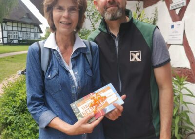 ein Mann und eine Frau lachen in die Kamera, die Frau hält einen Gutschein in der Hand.