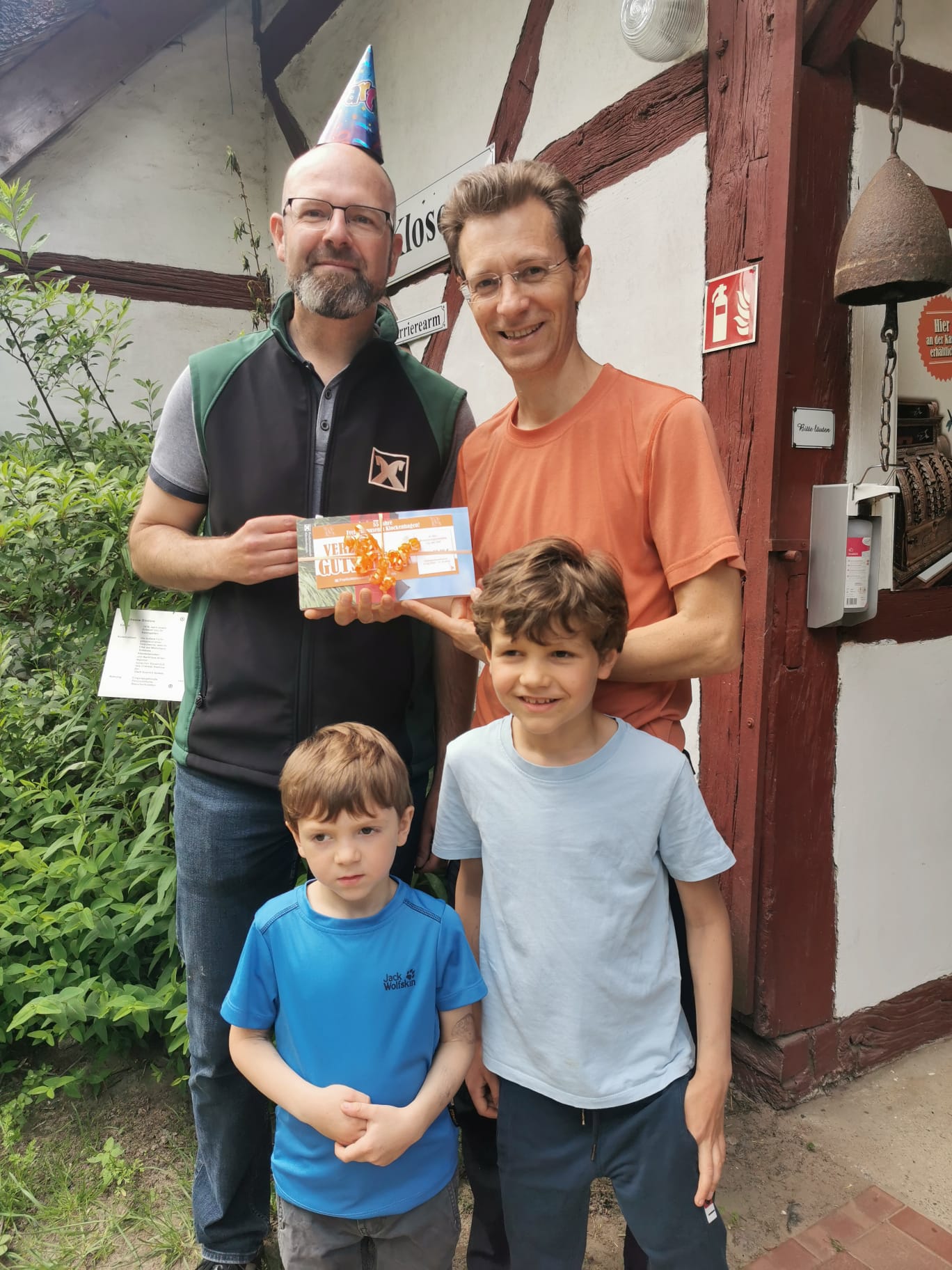 55. Museumsgeburtstag Zwei Männer und zwei Kinder lachen in die Kamera, ein Mann überreicht dem anderen Mann einen Gutschein.